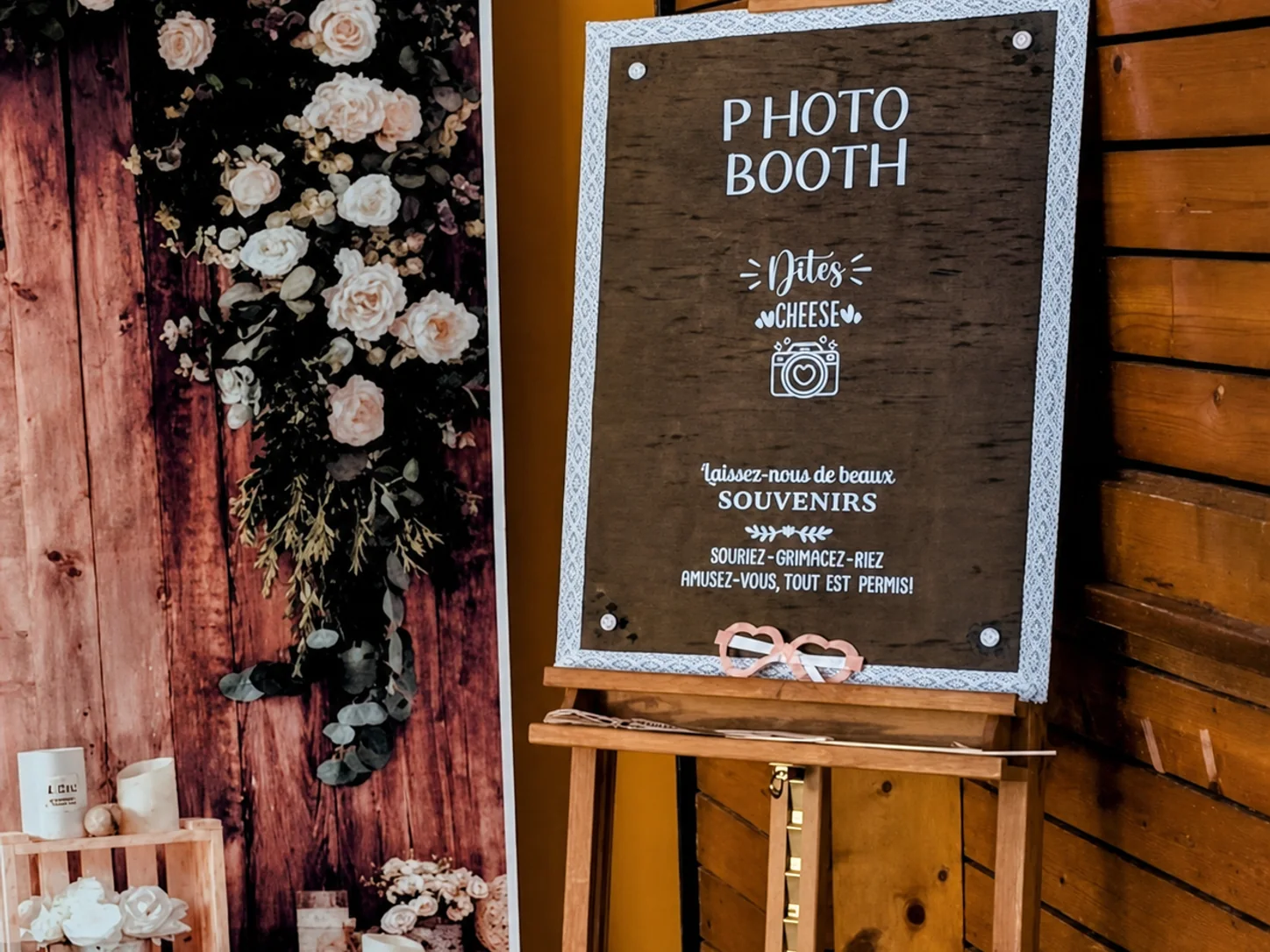Un panneau Photo Booth sur un chevalet, installé à côté d'un décor floral en intérieur.